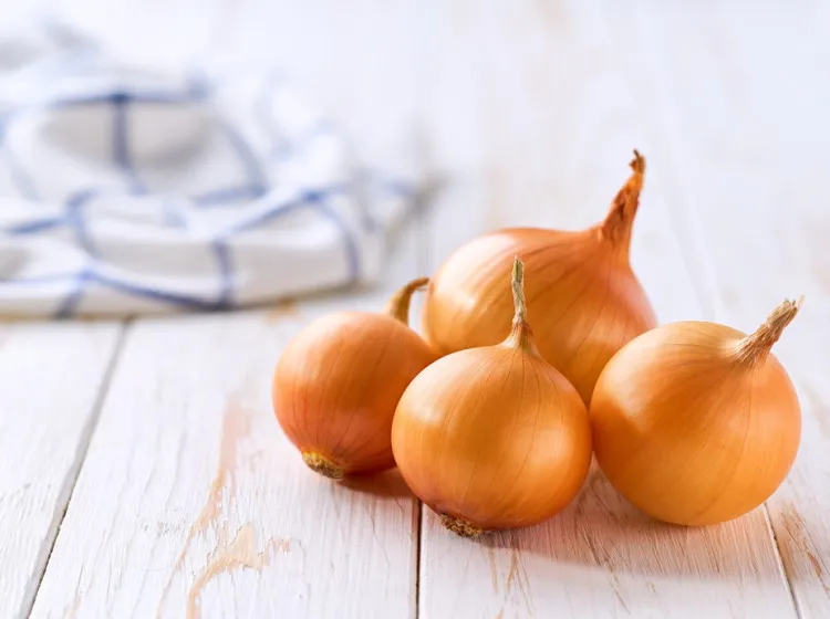 Čtyři celá žlutá cibule na bílém dřevěném povrchu.
