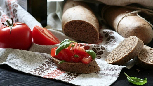 Hotová obložená bageta s rajčaty na bílém ubrusu.