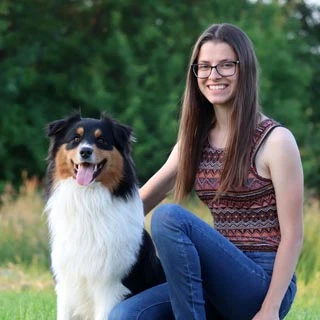 Dívka sedí s australským pastevcem na trávníku.