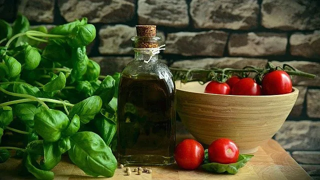 Čerstvá bazalka, rajčata a olivový olej na dřevěném prknu
