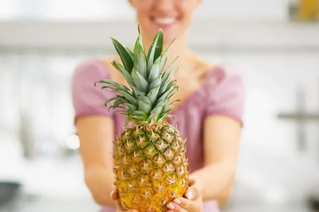 Žena drží čerstvý ananas v kuchyni.