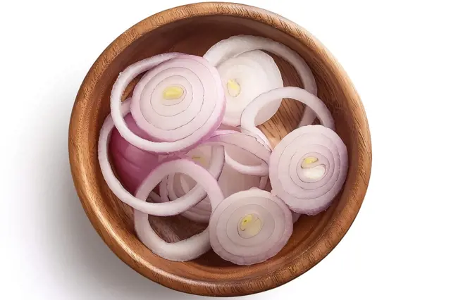 Rozkrojená červená cibule v dřevěné misce.