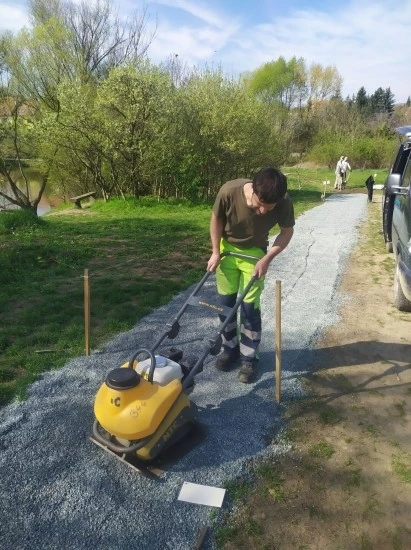 Muž utěsní štěrku pro trávník pomocí vibrační desky.