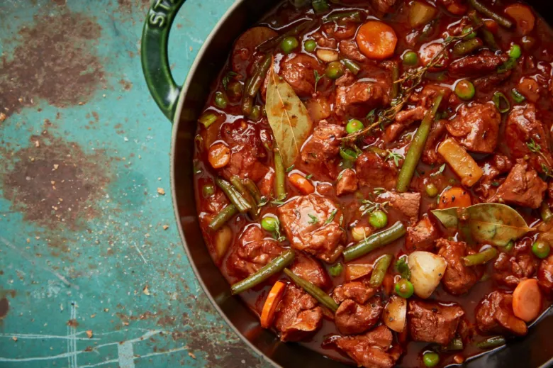 Hot venison goulash with vegetables and herbs in a cooking pot.