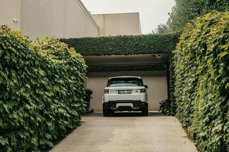 Bílý automobil v parkovišti obklopeném zelenou živou zdí.