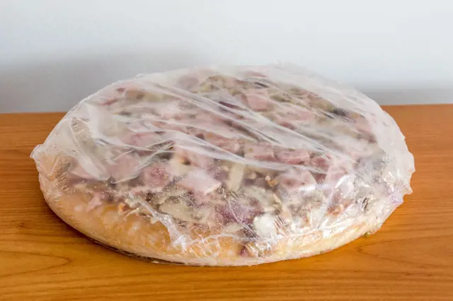 Mražená pizza zabalená v potravinářské fólii na dřevěném povrchu.