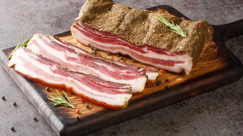 Křupavá slanina s bylinkami na dřevěném talíři.