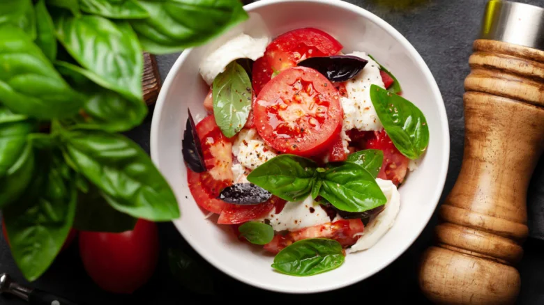 Salát caprese s bazalkou, rajčaty a mozzarellou v bílé misce.