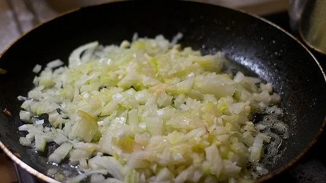 Smažená nakrájená cibule na pánvi.