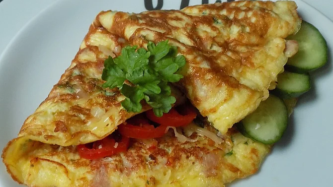 Připravená omeléta se šunkou a okurkou na talíři.