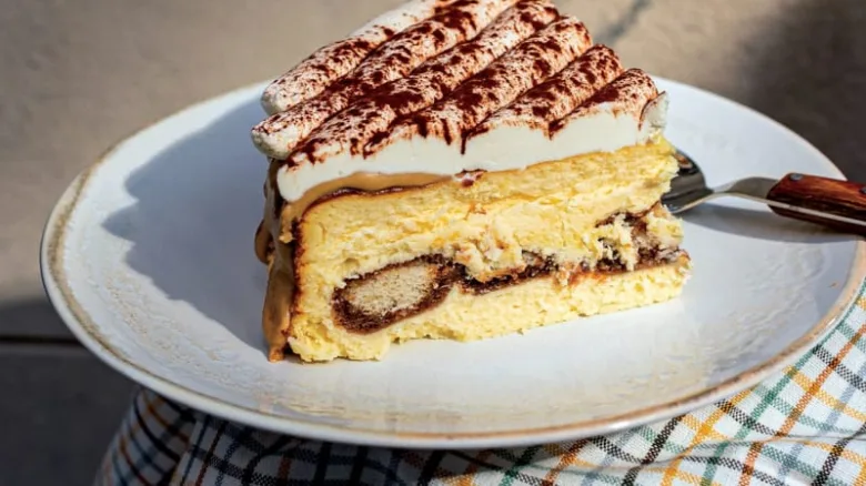 Kousek klasického italského dezertu tiramisú na bílém talíři.