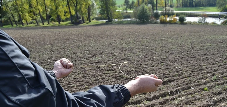 Muž hledá vodu proutkem nad oranou půdou.