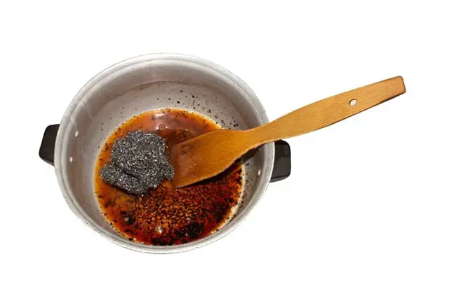 Připálenina v hrnci s dřevěnou lžící na bílém pozadí.