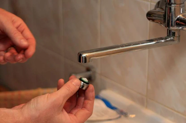 Ruce odšrouvají perlator z kohoutku v koupelně.