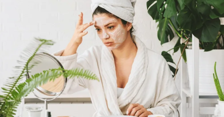 Žena nanáší domácí obličejovou masku před zrcadlem.
