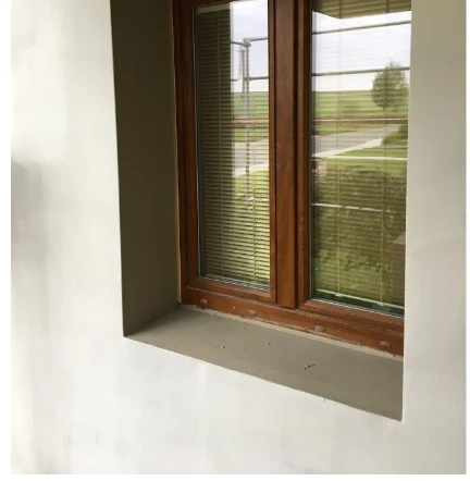 Detail parapetu pod oknem s dřevěným rámem a bílými stěnami.