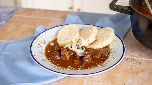 Hot venison goulash with dumplings and onion slices.
