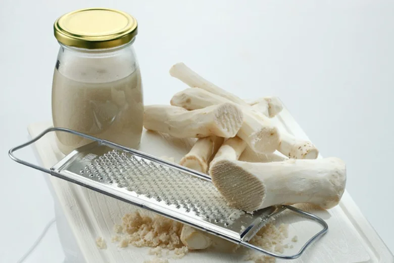 Čerstvý křen, struhadlo a připravený pastový produkt v sklenici.