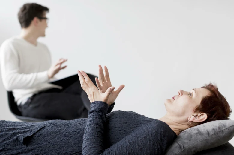 Žena leží na pohovce u terapeuta při psychoterapii.