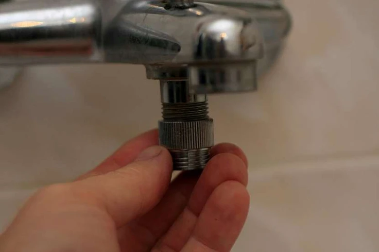 Ruka drží vyjmutý perlator z kohoutku na dlažbě.