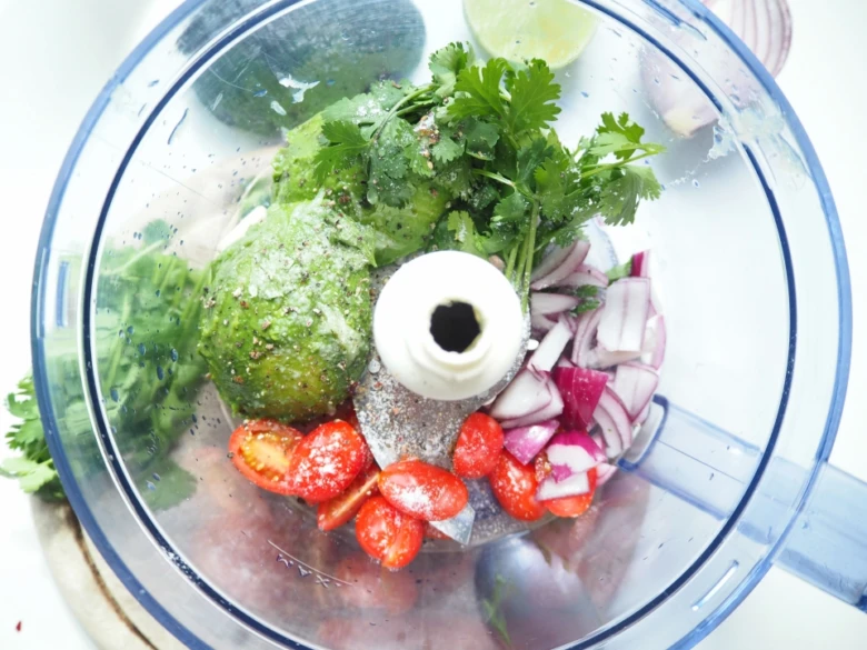 Ingredience pro guacamole v mixéru: avokádo, rajčata a cibule.