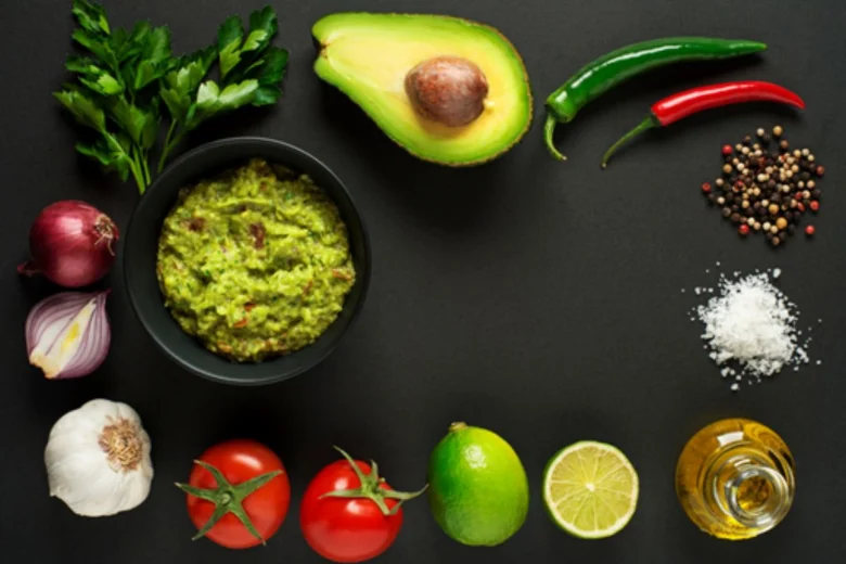 Čerstvé ingredience pro guacamole s hotovou směsí v černé mísce.