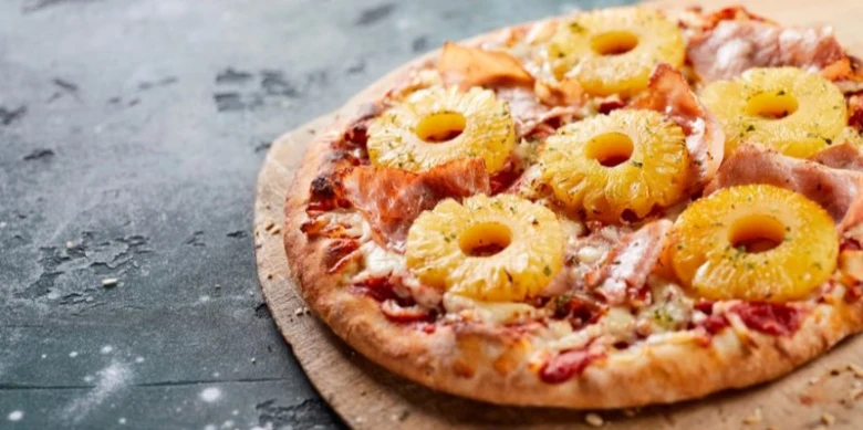 Pizzu s ananasem a šunkou na tmavém pozadí.