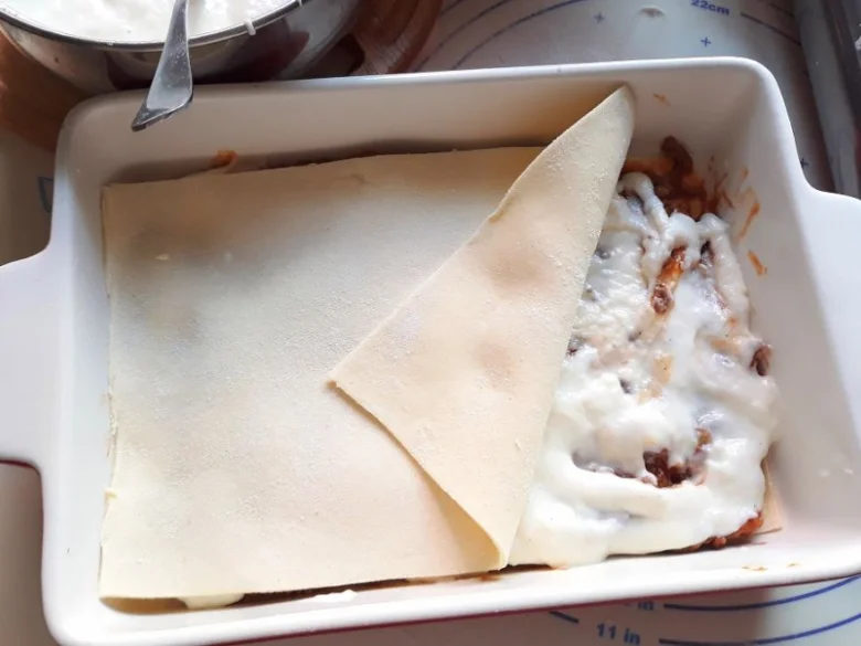 Příprava bezlepkového lasagne s vrstvami těsta, masa a sýra.
