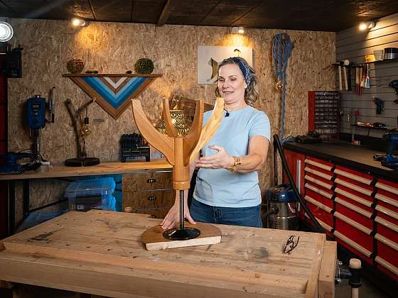 Žena v dílně s dřevěnou sochou na pracovním stole.